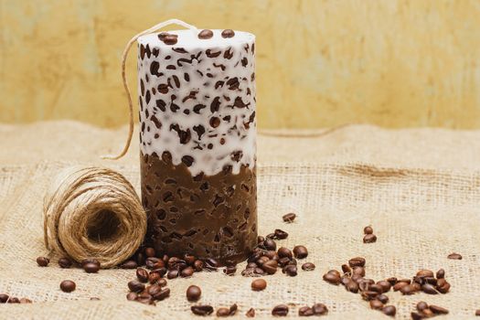 Beautiful Decorative Handmade candle with coffee beans on old sackcloth background. Candlelight.