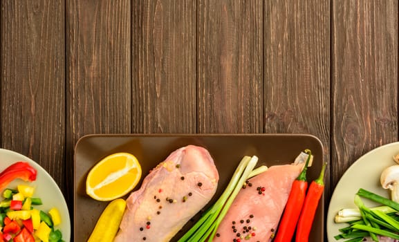 The chicken fillet and vegetables prepared for frying on a brown wooden background. Top view, copy space.