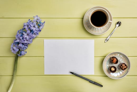 Paper, a pen, cup of black coffee and flowers on a wooden background. Top view. Copy space.