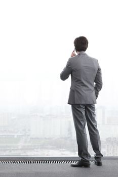 Businessman standing near window, looking at city and talking by phone
