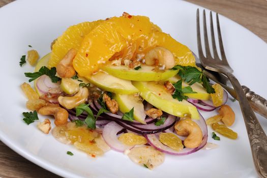 Salad with slices of orange, apple, blue onion, raisin, nuts, cashew nuts, herbs and honey sauce