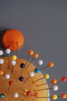 orange thimble and multicolored pins on the gray background top view macro shot