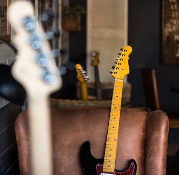 Detail of Electric Guitar Neck Leaning Agaist Leather Seat. Other Necks in Background and Foreground.