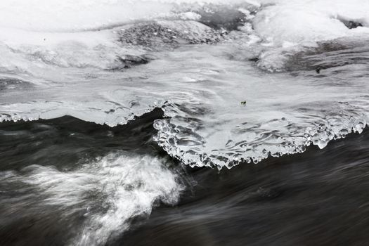 Icy ornaments on a small stream, black water