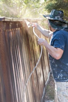 Professional Painter Spraying House Yard Fence with Wood Stain.