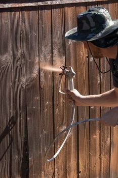 Professional Painter Spraying House Yard Fence with Wood Stain.
