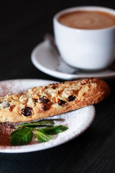 Cake on plate near cup of coffee on dark wooden table