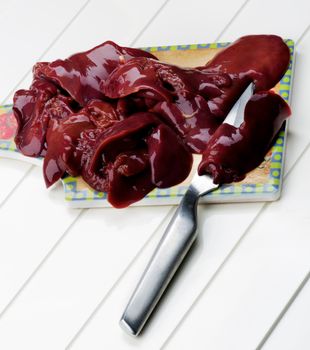 Fresh Raw Chicken Liver with Kitchen Knife on Cutting Board closeup on White Plank background