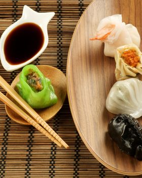 Assorted Dim Sum on Wooden Plates and Soy Sauces with Chopsticks closeup on Straw Mat background