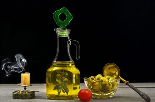 Olive oil, olives and tomatoes on wooden surface and black background. Smoke candle.