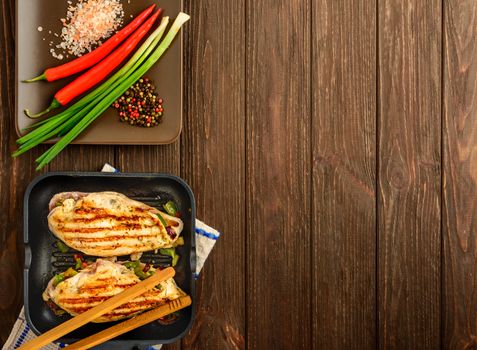 The juicy chicken fillet and vegetables made on a grill on a brown wooden background. Flat lay, copy space.
