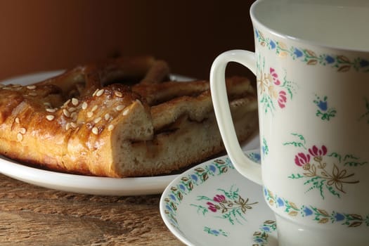 Beautiful white porcelain cup painted with flowers and a piece of sweet cake with sesame seeds