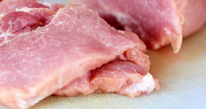 Raw pork meat slices on white cutting board.