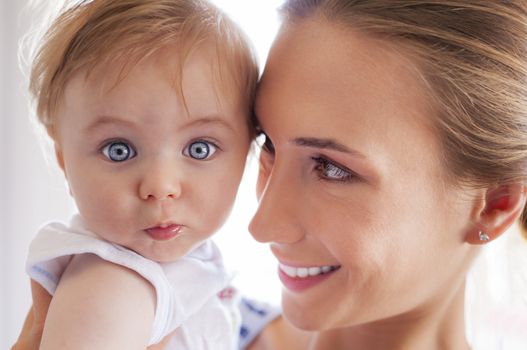 A beautiful young mother embracing her little baby boy with big curious eyes.