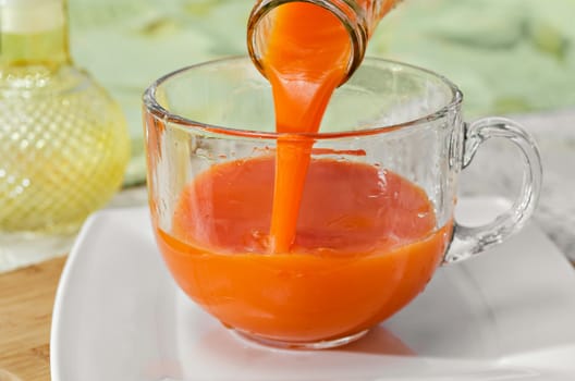 Carrot juice is poured from the bottle into the Cup, which stands on the table and a white plate. Selective focus.