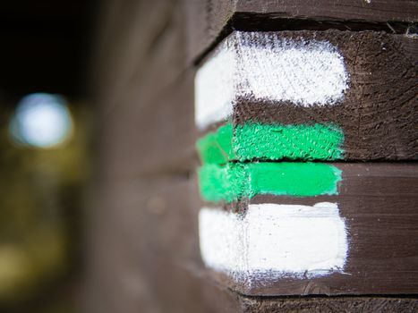 Green and white hiking arrow sign on wooden wall corner, typical for czech tourism, providing guidence, touristic navigation or directions, copyspace with blurred background