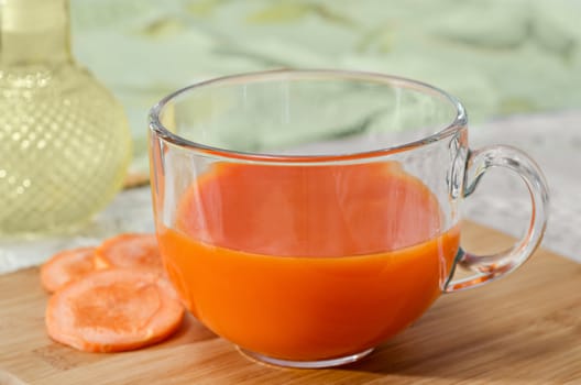 Fresh carrot in the Cup, which stands on the table and the cutting Board, slices of carrots nearby. Selective focus.