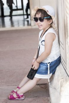 Portrait of a happy little girl laughing and leaning on the wall outdoors.