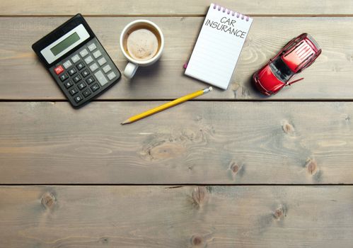 Notepad with car insurance handwritten on a table with a miniature car 