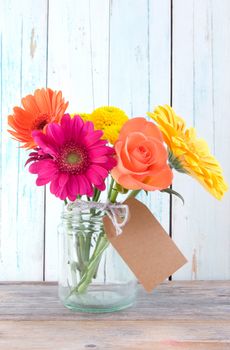 Bunch of flowers with blank gift label on wooden background
