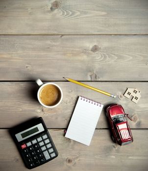 Blank notepad on a wooden table with a miniature car and house 