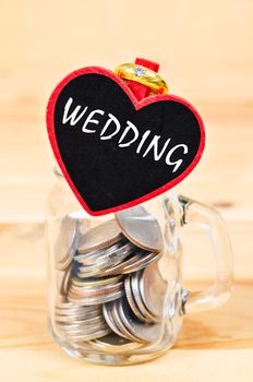 Savings in glass bank and Wedding Ring on wooden background.