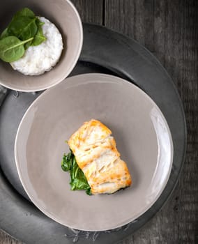 Fried cod fillets and spinach served on a wooden surface