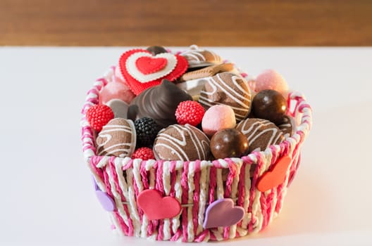 Sweets, biscuits and decorative hearts for Valentine's day in a beautiful basket, on a white surface. Selective focus, space for text.