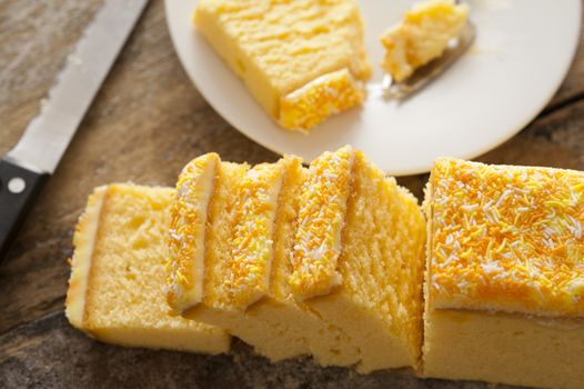 Sliced iced vanilla sponge cake on a cutting board with a knife and a plate with a single slice in the process of being eaten