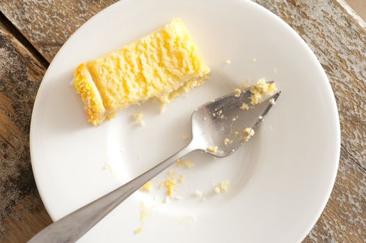 Half eaten slice of yellow sponge cake on a plate with a spoon and crumbs viewed from above