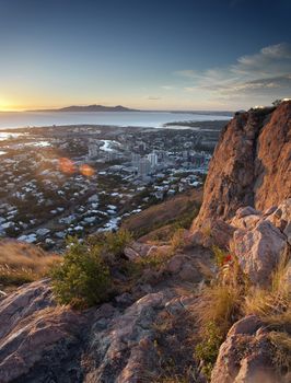 Overview of Townsville, Queensland, Australia from a lookout on a mountain peak over the rooftops of the city to the ocean beyond at sunset