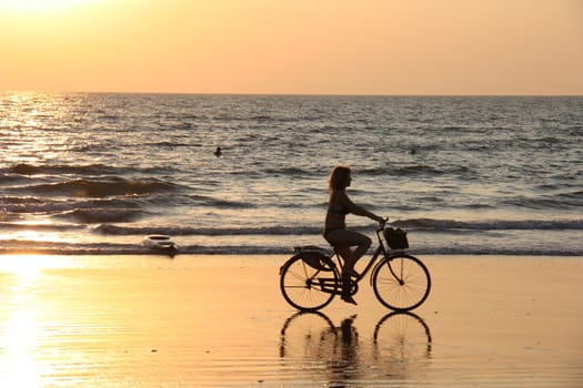 A girl rides a Bicycle along the shore at sunset