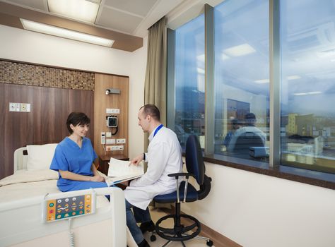 A doctor is bringing good news to a young female patient in modern hospital room.