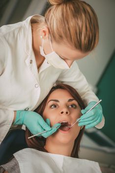 Beautiful young woman at visit in the dentist office. She is sitting on a chair and female dentist checkup teeth on her. Selective focus.