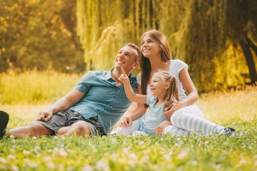 Happy smiling family sitting on the grass in the park and looking up.