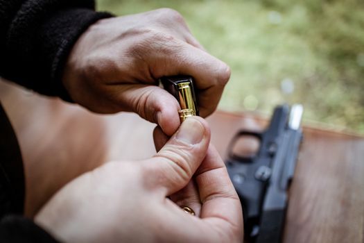 Close-up of a man hands holding and loading 9mm bullets in the pistol at the shooting range.