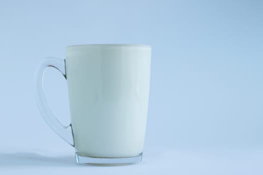 Full transparent glass poured milk on light white and blue background