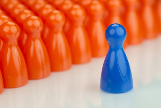 Conceptual orange game pawns and a blue play pawn as abstract display of inequality in color and number of
