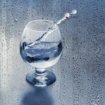 Clean water in a glass and splash on the background of the drops. Cropping into a square, place for text.