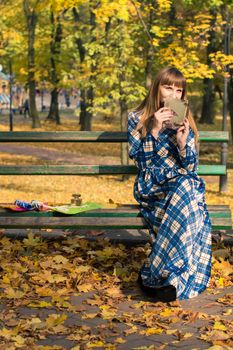 beautiful girl with long straight hair in a blue long dress reading a book in the autumn park