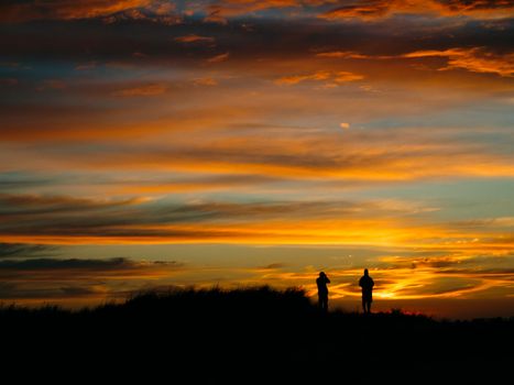 Silhouette of two people looking the sunset beach.