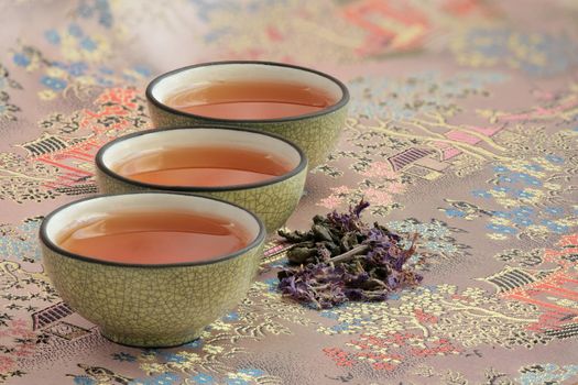 three cups filled with tea on a beautiful tablecloth and a pinch of fragrant flower tea