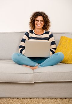 Beautiful woman at home sitting on the sofa working with a laptop