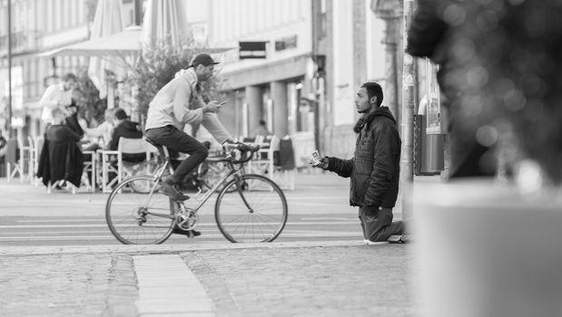 INNSBRUCK, AUSTRIA – NOVEMBER 1st 2015: Refugee begging for help in the streets of Innsbruck with people walking by.