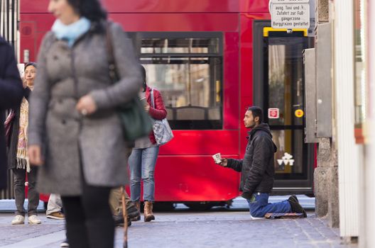 INNSBRUCK, AUSTRIA – NOVEMBER 1st 2015: Refugee begging for help in the streets of Innsbruck with people walking by.