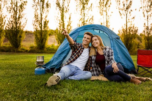 Shot of a happy couple camping on the nature and pointing to somewhere