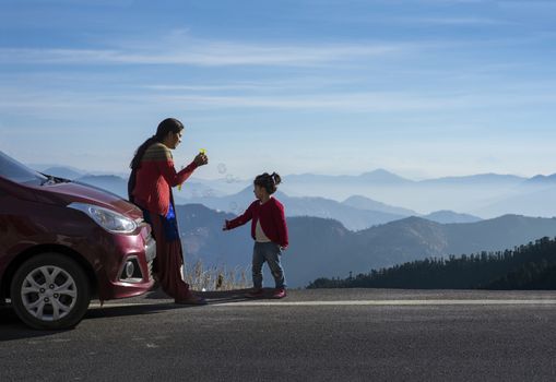 Mother and daughter enjoying the road trip and winter vacation in Shimla, Himachal Pradesh, India. Car travel vacation concept photo against Himalayan mountain in the background.