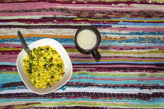 Bowl of poha(Flattened rice/beaten rice/Pounded paddy) and a mug of coffee on colorful rug, top view.