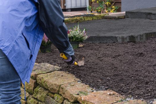 Woman with work gloves and garden tools while planting a flower bed in autumn. agriculture concept
