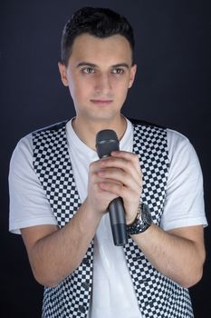 Young black-haired man dressed in black and white performs singing to microphone